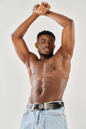 Shirtless African American man with hands on head, deep in thought, in a studio setting against a grey background.
