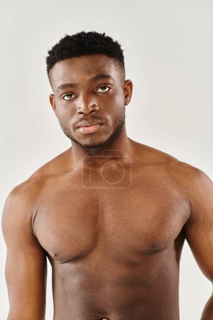 A young, shirtless African American man strikes a pose of serenity in a studio against a grey background.