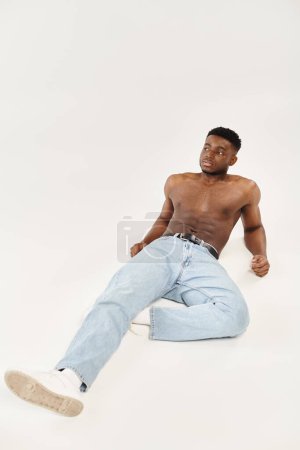 Junger schwarzer Mann mit durchtrainiertem Körperbau sitzt in einem Studio auf dem Boden und strahlt Zuversicht und Entspannung aus.