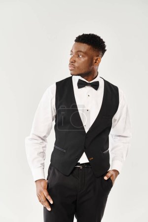 Ein junger, gutaussehender afroamerikanischer Bräutigam posiert selbstbewusst in einem eleganten Smoking vor grauem Studiohintergrund.