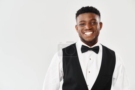 Handsome African American groom smiles joyfully at the camera, exuding charm in a stylish tuxedo against a grey studio backdrop.