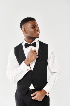 A young, handsome African American groom in a tuxedo poses for a picture in a studio setting against a grey background.
