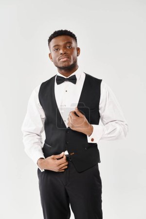 A young African American man in a stylish tuxedo strikes a sophisticated pose for a portrait on a gray studio background.