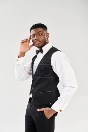 A young, handsome African American man in a tuxedo strikes a confident pose in a studio setting against a grey background.
