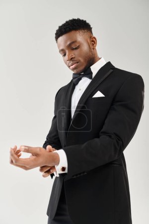 Handsome African American groom in a stylish tuxedo, calmly holding his hands together, exuding class and sophistication.
