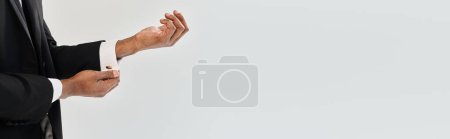 Photo for Handsome African American groom in suit and tie holding hands together in a graceful and poised gesture on a grey background. - Royalty Free Image
