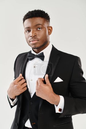 A young and handsome African American groom in a tuxedo striking a confident pose in a studio setting against a grey background.