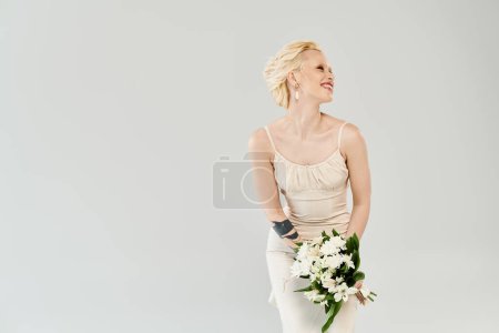 Téléchargez les photos : Une belle mariée blonde dans une robe de mariée tenant un bouquet de fleurs, exsudant sérénité et élégance. - en image libre de droit
