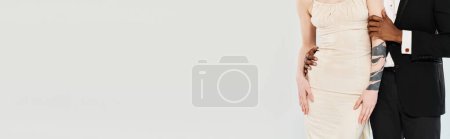 Photo for A beautiful blonde bride in a wedding dress and an African American groom standing next to each other in a studio on a grey background. - Royalty Free Image