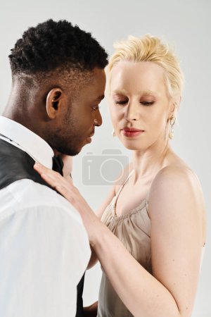 A beautiful blonde bride in a wedding dress standing next to an African American groom in a studio on a grey background.