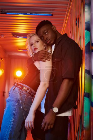 Foto de Una mujer rubia y un hombre afroamericano se paran uno al lado del otro en una calle urbana con coloridos grafitis en las paredes. - Imagen libre de derechos