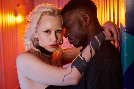 A blonde woman and African American man share a warm embrace on an urban street adorned with colorful graffiti.