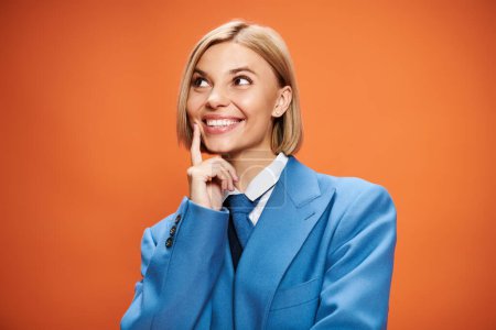 Foto de Mujer atractiva alegre con pelo rubio en elegante atuendo elegante posando sobre fondo naranja - Imagen libre de derechos