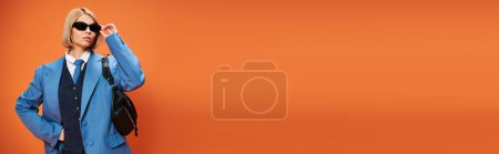 Photo for Appealing woman with short hair in chic attire with sunglasses posing on orange backdrop, banner - Royalty Free Image
