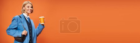 Photo for Happy sophisticated woman with blonde short hair holding purse and coffee on orange backdrop, banner - Royalty Free Image