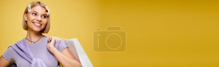 Téléchargez les photos : Femme heureuse avec des accessoires en tenue chic posant avec sac à provisions sur fond jaune, bannière - en image libre de droit