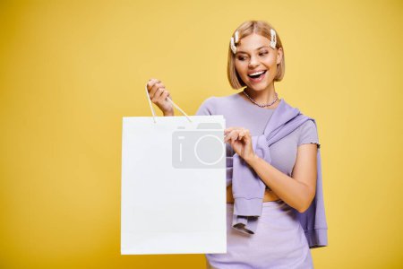 Foto de Mujer atractiva alegre con accesorios en traje elegante posando con bolsa de compras sobre fondo amarillo - Imagen libre de derechos