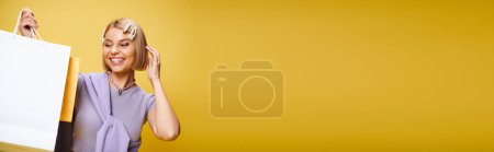Foto de Alegre mujer de buen aspecto con el pelo corto posando sobre fondo amarillo con bolsas de compras, pancarta - Imagen libre de derechos