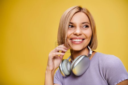 Foto de Encantadora mujer alegre con pelo corto y rubio y auriculares disfrutando de la música en el fondo amarillo - Imagen libre de derechos