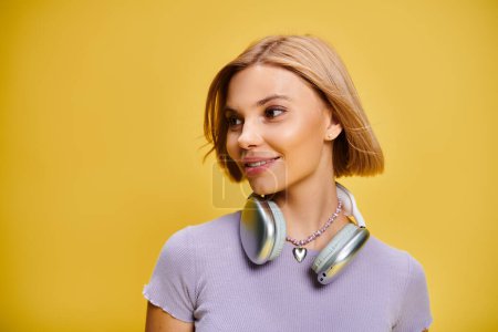 Foto de Mujer alegre de buen gusto con pelo corto rubio y auriculares disfrutando de la música en el fondo amarillo - Imagen libre de derechos
