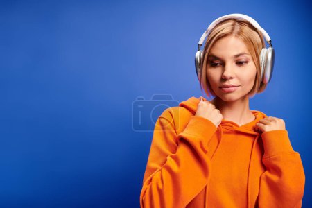 Foto de Hermosa mujer alegre con pelo corto y rubio y auriculares disfrutando de la música en el fondo azul - Imagen libre de derechos