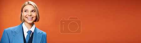 Téléchargez les photos : Jolie femme joyeuse avec les cheveux courts en tenue sophistiquée posant sur fond orange heureusement, bannière - en image libre de droit