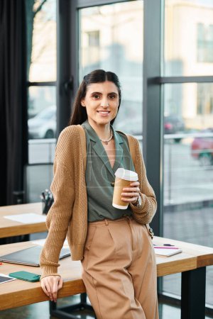 Una mujer está de pie con confianza frente a una mesa en un entorno de oficina corporativa, sosteniendo pacíficamente una taza de café.