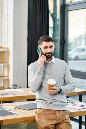 A man in a business setting holds a cup of coffee while talking on a cell phone.