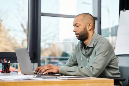 Un hombre en una oficina corporativa se sienta en su escritorio, intensamente enfocado en la pantalla de su computadora portátil mientras trabaja en un proyecto.