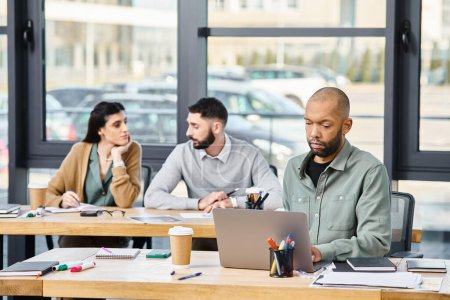 Drei Personen treffen sich in einem produktiven Meeting, kauern um einen Laptop und diskutieren ein Projekt in einem modernen Büroumfeld..