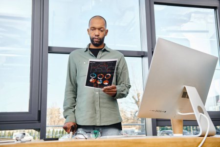 Un hombre en una oficina de pie ante un gran monitor de computadora, inmerso en el trabajo en un proyecto para su negocio.