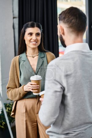 Eine Frau und ein Mann unterhalten sich lässig, während er in einem Büro eine Tasse Kaffee hält.