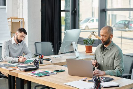 Dos hombres de negocios se sientan en una mesa, inmersos en sus computadoras portátiles, haciendo una lluvia de ideas y colaborando en un proyecto en un entorno de oficina moderno, inclusivo