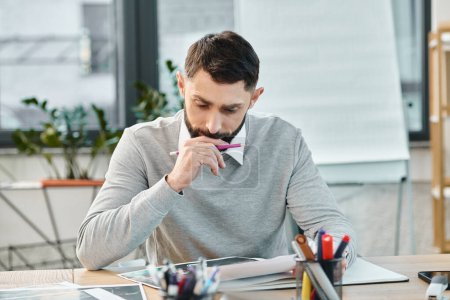 Ein Mann sitzt an einem Schreibtisch, in ein Blatt Papier vertieft, tief in Gedanken, umgeben von der Hektik eines Firmenbüros.