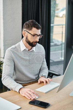 Téléchargez les photos : Un homme assis à un bureau, profondément absorbé par le travail, utilisant un ordinateur pour naviguer dans un projet pour une mission d'entreprise. - en image libre de droit