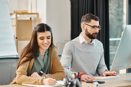Un homme et une femme, faisant partie d'une équipe d'entreprise, sont assis à un bureau, collaborant sur un ordinateur pour travailler sur un projet dans leur bureau.