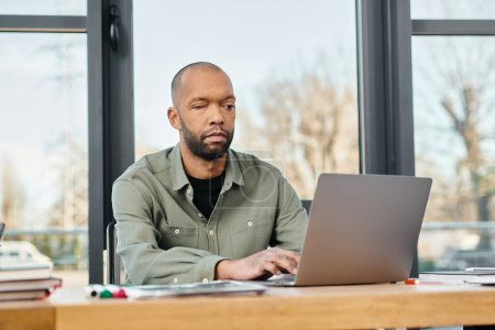 Un homme atteint de myasthénie grave assis à un bureau, concentré sur son écran d'ordinateur portable, travaillant sur un projet dans un cadre de bureau moderne.