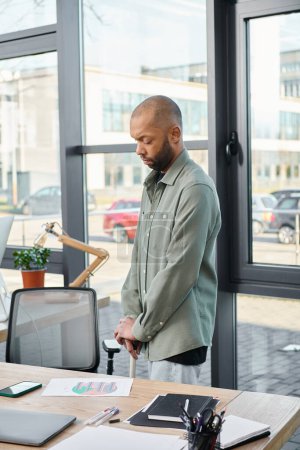 Foto de Un hombre con miastenia gravis en un entorno de oficina moderno, de pie con confianza frente a una computadora portátil, absorto en su trabajo. - Imagen libre de derechos