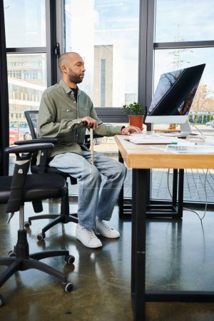 disabled african american man with myasthenia gravis in corporate attire sits focused at a desk, typing on a computer screen among office supplies.