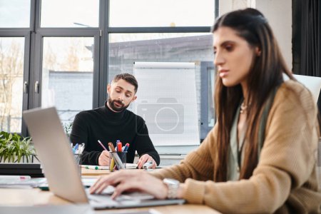 Photo for A man and a woman immersed in work at a table, focused on a laptop screen in a professional office setting. - Royalty Free Image
