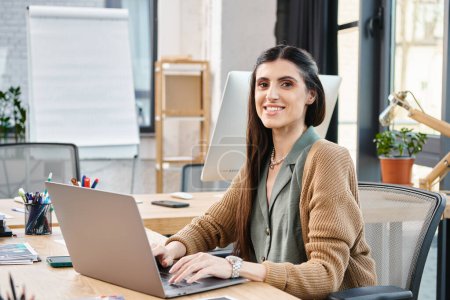 Eine professionelle Frau mit langen Haaren sitzt an einem Schreibtisch und konzentriert sich auf ihren Laptop, während sie in einem Büro arbeitet.