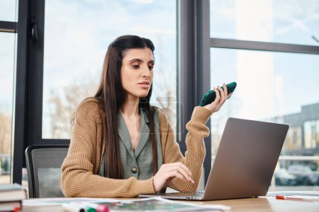 Una mujer sentada en un escritorio, absorta en su trabajo, usando una computadora portátil en un entorno de oficina corporativa.