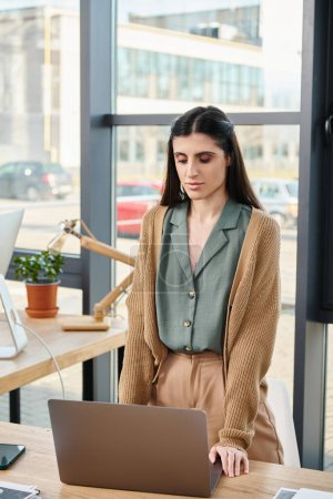 Une femme debout devant un ordinateur portable dans un bureau, concentrée et engagée dans son travail.