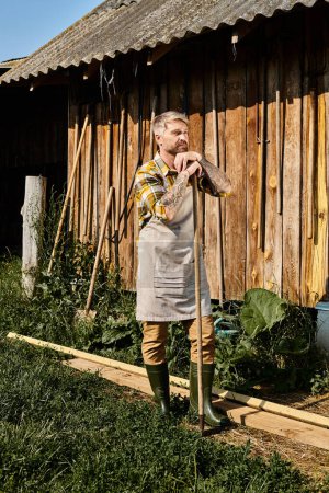 schöner engagierter Bauer in lässiger Kleidung mit Mistgabel bei der Arbeit mit Heu im Dorf
