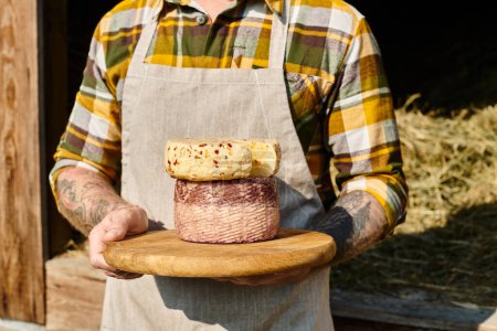 Ausgeschnittene Ansicht eines erwachsenen Bauern mit Tätowierungen in Freizeitkleidung, der selbst gemachten Käse in den Händen hält