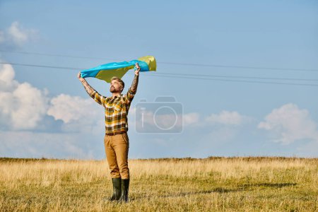 appealing Ukrainian man in casual attire posing with national flag, scenic landscape, modern farmer