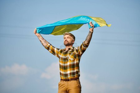 appealing Ukrainian man in casual attire posing with national flag, scenic landscape, modern farmer