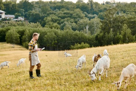 granjero moderno de buen aspecto con barba y tatuajes usando portapapeles para analizar su ganado de cabras