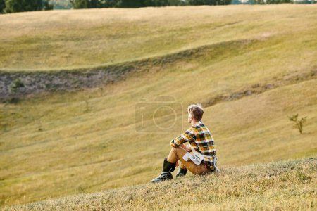 gutaussehender engagierter Mann mit Bart entspannt auf grünem Frühlingsfeld und schaut weg, moderner Bauer
