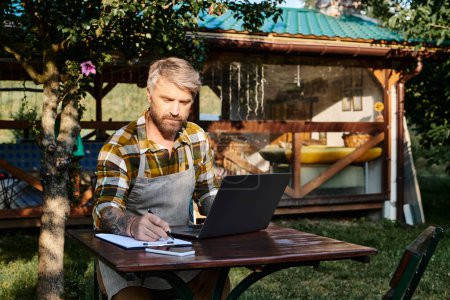 hombre guapo trabajador con barba usando el ordenador portátil y portapapeles para analizar los recursos en la granja